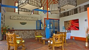 Un patio espacioso con mecedoras y mesas de madera, un muro de piedra y un ventanal con contraventanas azules.