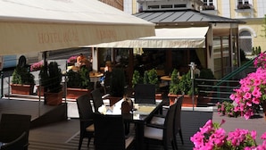 An outdoor seating area with tables and chairs, a building with a sign reading "HOTEL RÜZE," and a clear blue sky with clouds. - Hotel Ruze (Karlovy Vary)