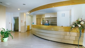 A reception area with a curved counter, a clock on the wall, and a potted plant. - Hotel Ruze (Karlovy Vary)