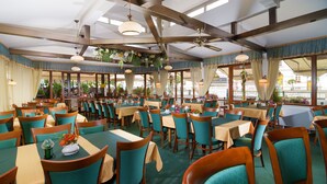 A restaurant with multiple tables and chairs, large windows, and hanging plants. - Hotel Ruze (Karlovy Vary)