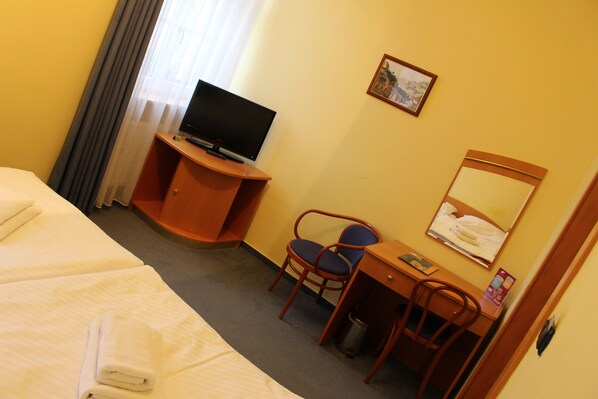A hotel room with two beds, a desk with a chair, a television, and a small trash can.