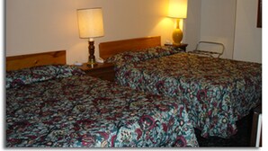 Habitación de hotel con dos camas, cada una con cubrecama estampado, una mesita de noche con lámpara y una pequeña mesa con una silla.