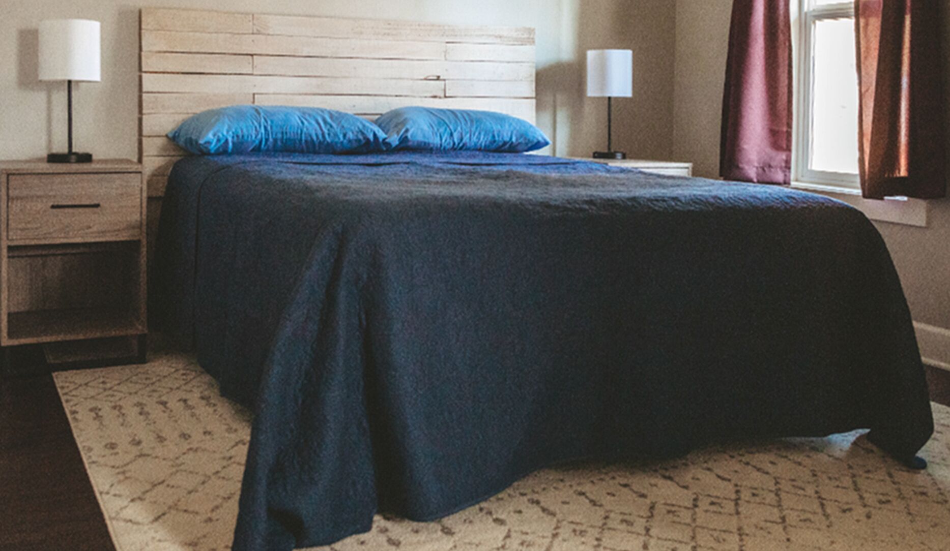 A bedroom with a bed, two bedside tables, and a window with curtains.