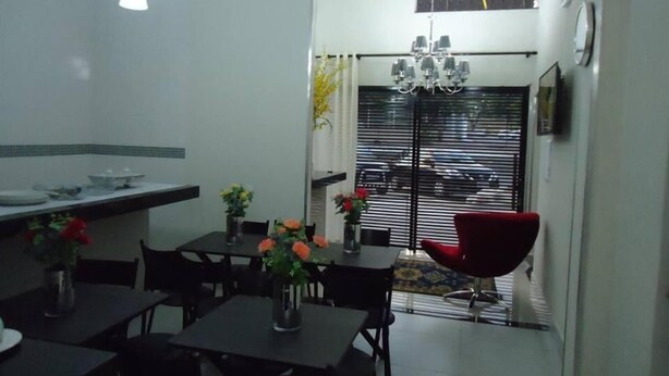 A compact kitchen with a dining area, featuring a chandelier, a red chair, and a view through a window with blinds. - Hotel MM (Nucleo Bandeirante)