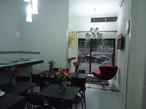 Cocina compacta con comedor, que incluye una araña, una silla roja y vistas al exterior a través de una ventana con persianas.