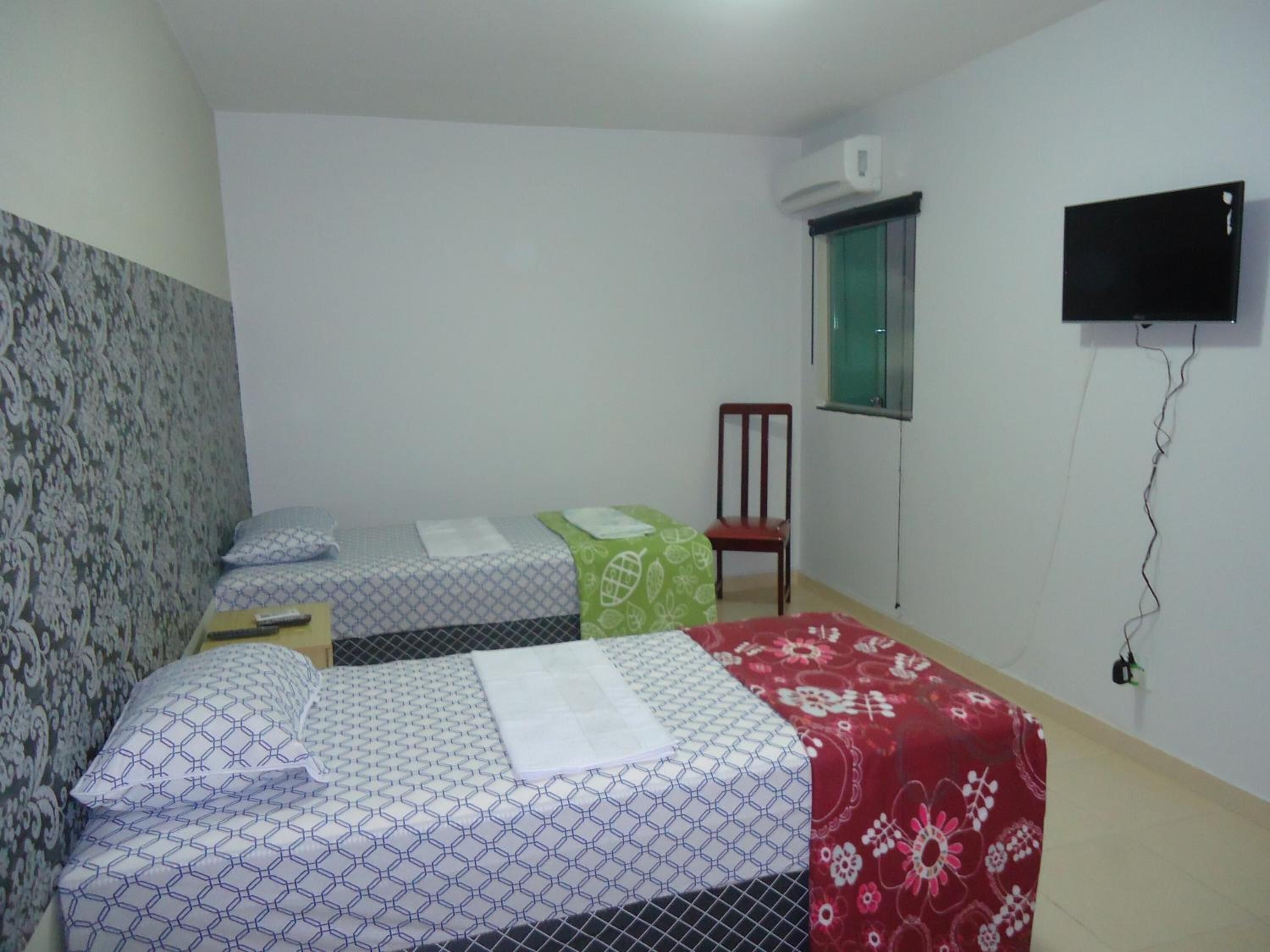 Una habitación con dos camas, una con cubrecama estampado y la otra con estampado floral. Hay una silla, una ventana con vistas y un televisor montado en la pared.