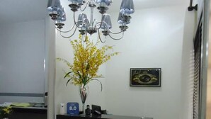 A hotel reception desk with a chandelier, a vase with yellow flowers, and a framed picture on the wall. - Hotel MM (Nucleo Bandeirante)