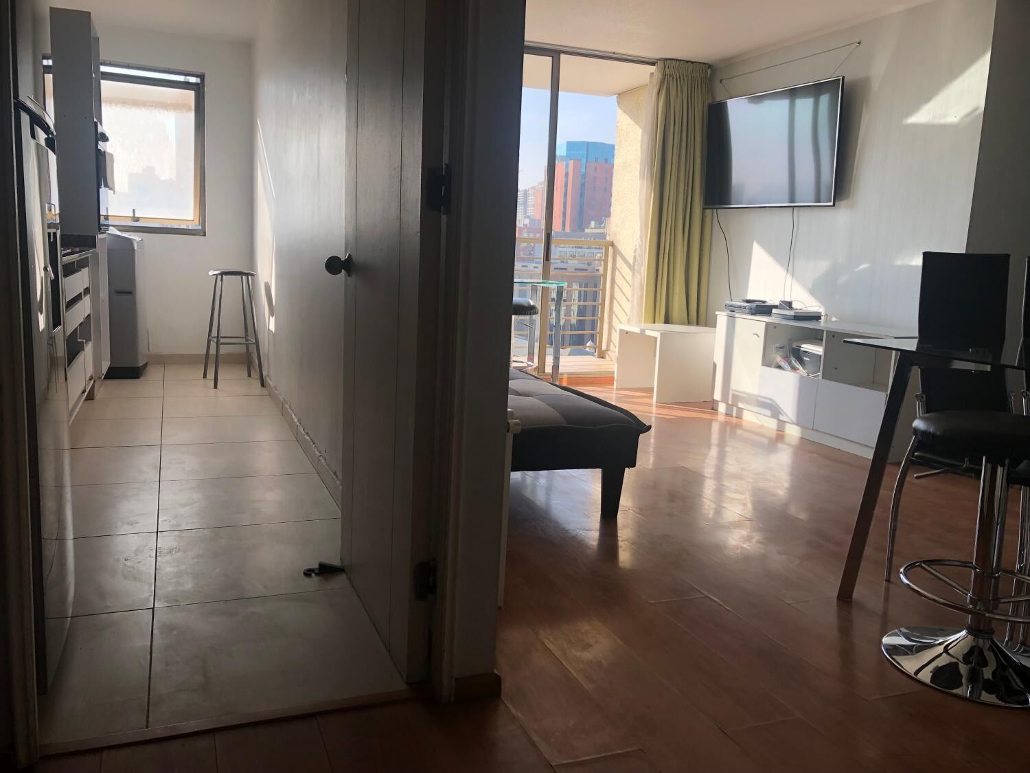 Un apartamento moderno con kitchenette, comedor, un amplio ventanal con vistas a la ciudad y un televisor montado en la pared.