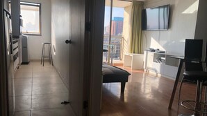 Um apartamento moderno com cozinha compacta, área de refeições, janela ampla com vista para a cidade e televisão na parede.