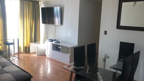 Uma sala de estar moderna com televisão de tela plana, mesa de jantar de vidro e sofá.