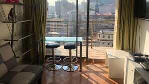 Uma sala de estar moderna com uma janela grande, um sofá, dois banquetes, uma mesa pequena e uma televisão.