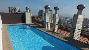Piscina no terraço com água azul cristalina, rodeada por um guarda-corpo metálico e vista para o horizonte urbano.