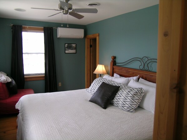 Un dormitorio con cama, ventilador de techo, equipo de aire acondicionado, ventana con cortinas y puerta.
