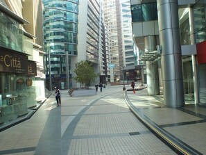 A modern urban plaza with high-rise buildings, a pedestrian walkway, and a small tree.