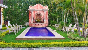 Un espace piscine agrémenté d’une fontaine, entouré de chaises et d’une végétation luxuriante.