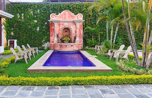 A pool area with a fountain, surrounded by chairs and lush greenery. - Casa Mia Hotel (Antigua Guatemala)