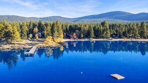 Una vista serena de un lago, con un muelle que se adentra en el agua, rodeado de un bosque denso y montañas al fondo.
