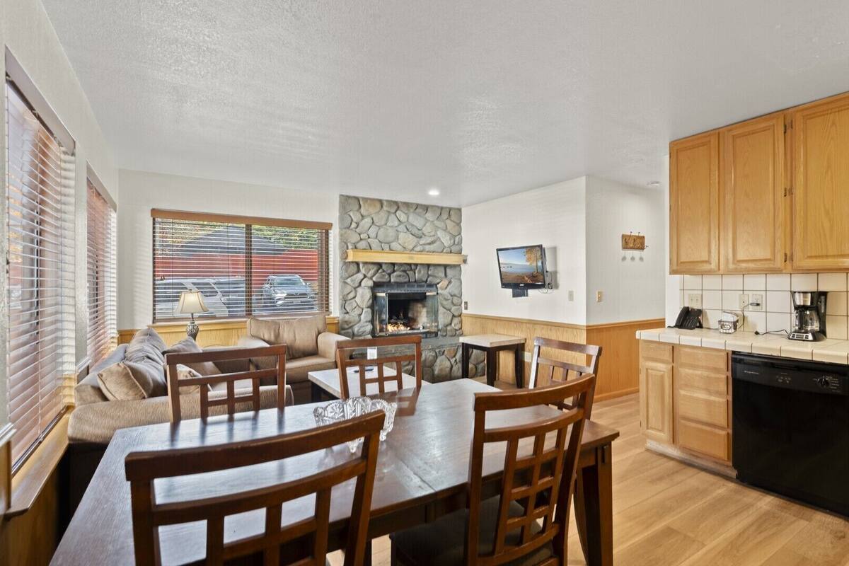 A cozy living area with a fireplace, a dining table with chairs, and a kitchen with wooden cabinets and a dishwasher.