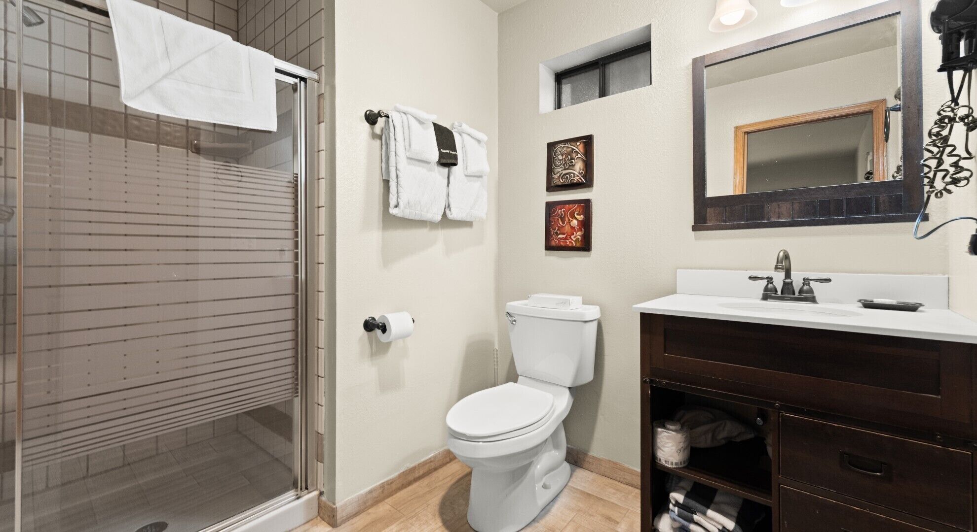 A bathroom with a glass shower enclosure, a toilet, a sink with a dark cabinet, and a mirror above the sink.