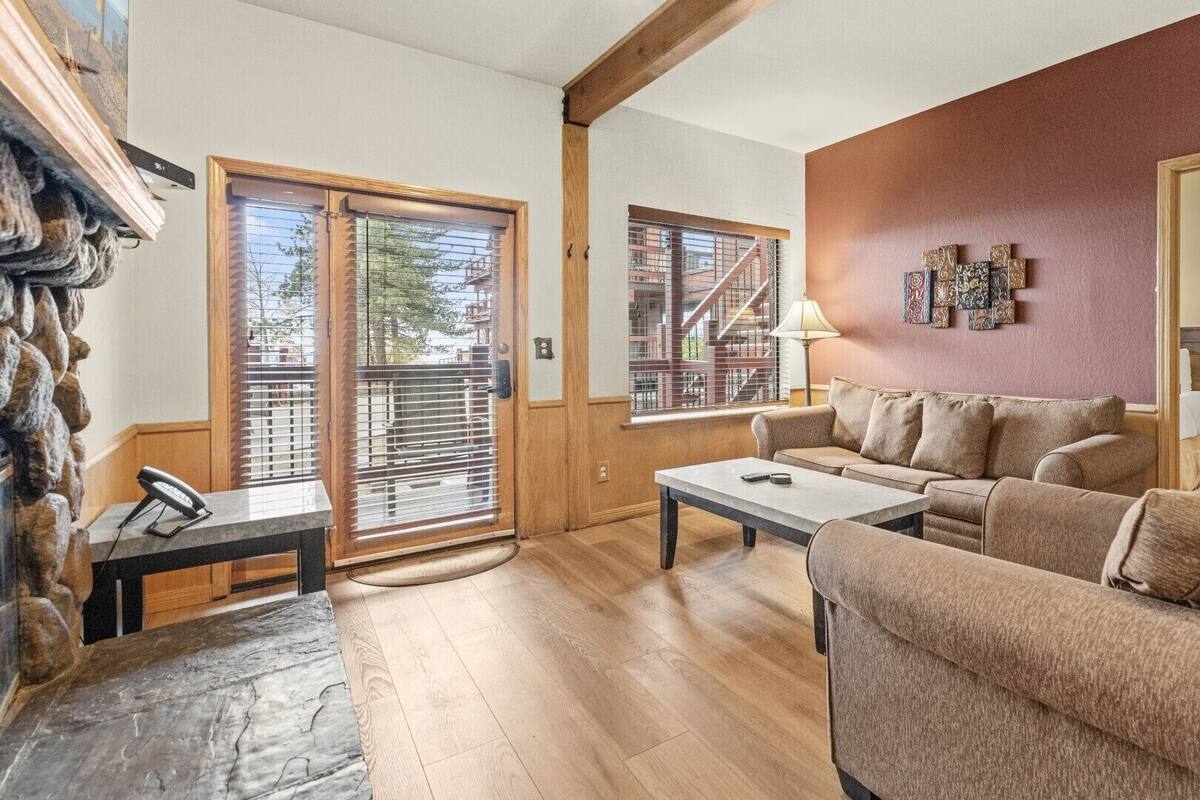 A cozy living room with a sofa, coffee table, and a fireplace. There are wooden floors and a stone wall.