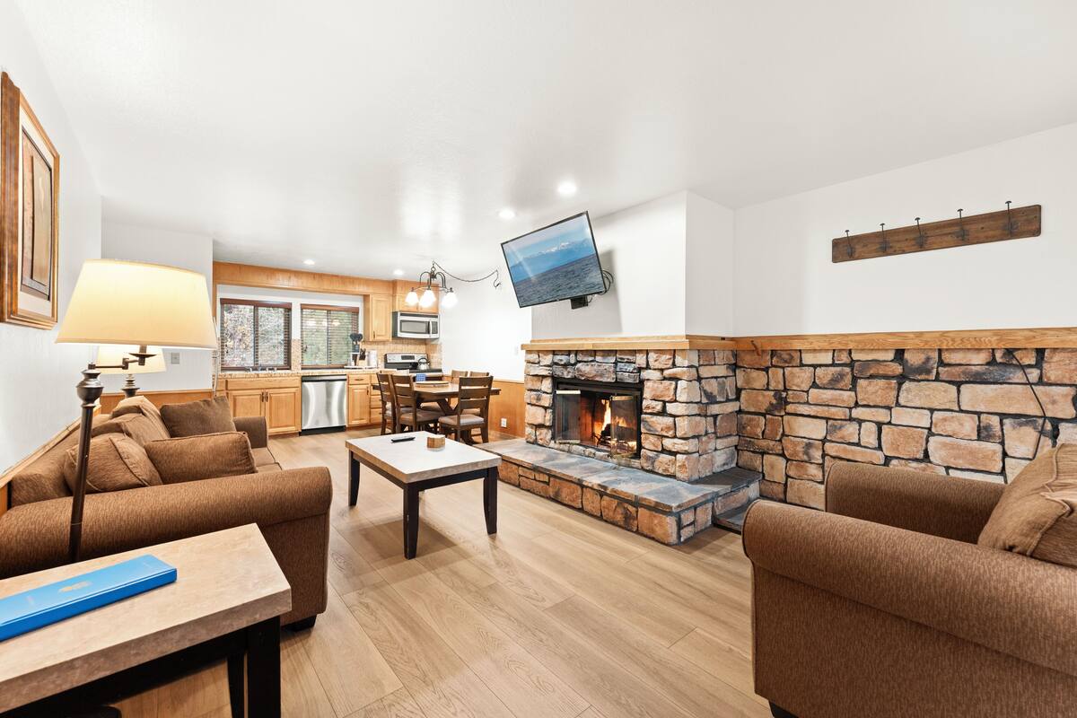 A living room with a stone fireplace, a television mounted on the wall, and a dining area with wooden furniture.