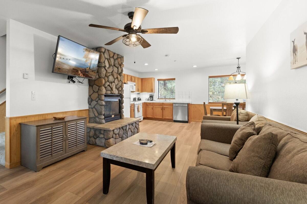 A modern living room with a stone fireplace, a flat-screen TV, a ceiling fan, and a cozy seating area.