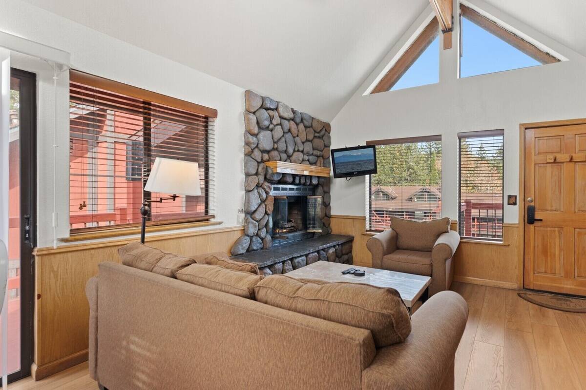 A cozy living room with a stone fireplace, a television mounted above it, and a comfortable seating area with a sofa and armchairs.