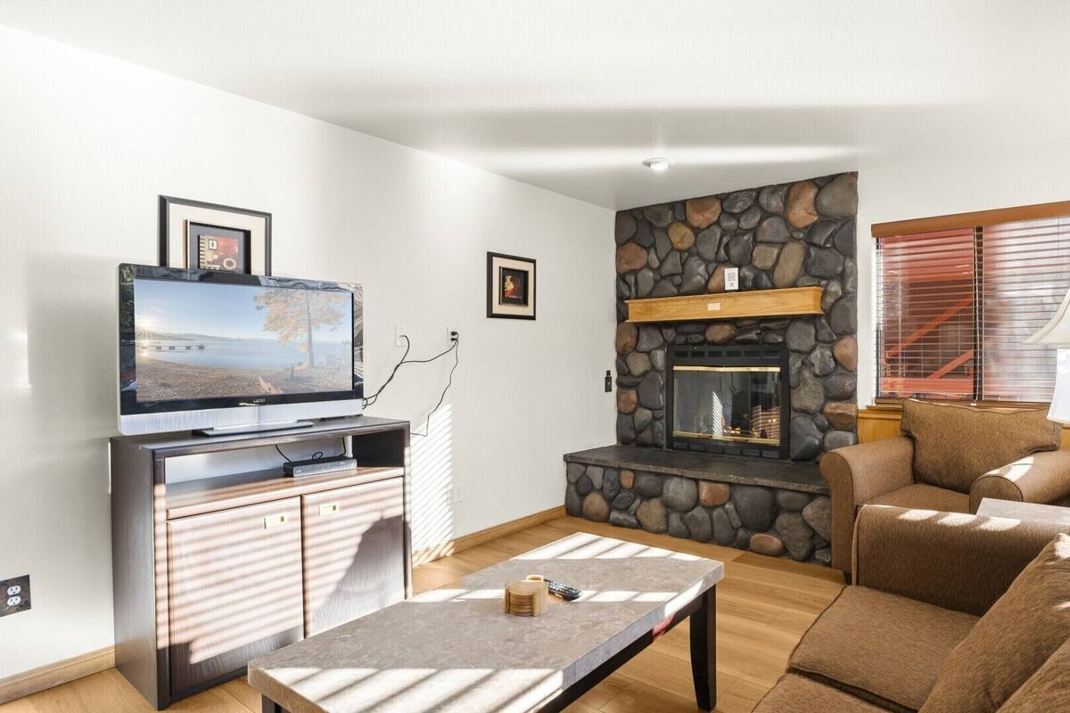 A living room with a stone fireplace, a television on a stand, a sofa, and a coffee table.