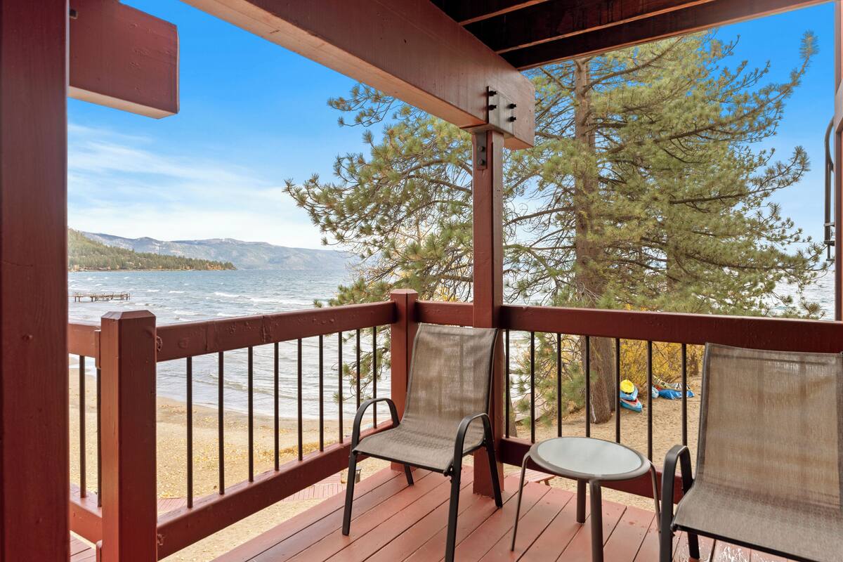 A wooden deck with two chairs and a table overlooking a lake with mountains in the background.