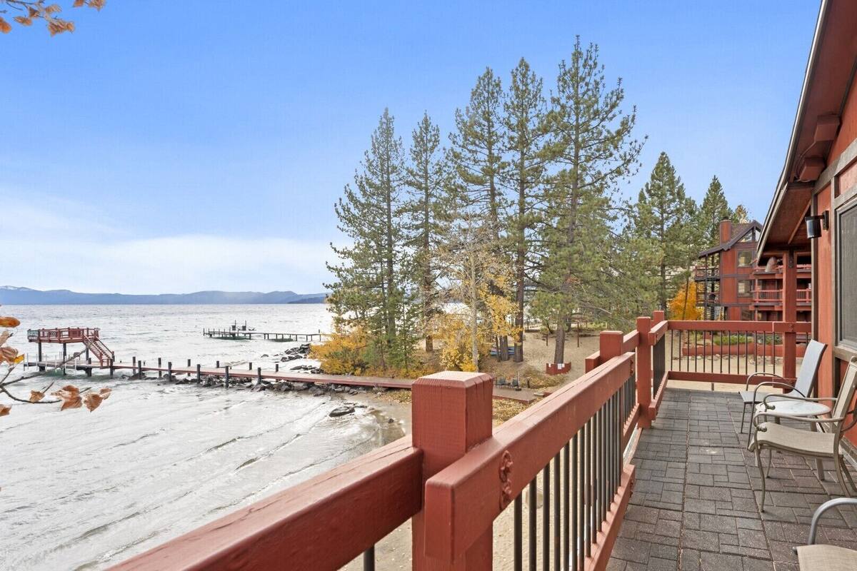 A wooden deck with a view of a lake, surrounded by trees and a building with large windows.