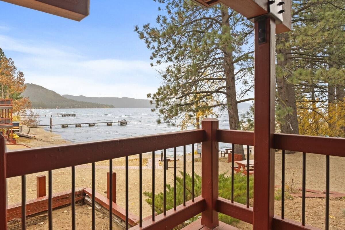A wooden deck with a metal railing overlooking a lake, with a dock extending into the water.