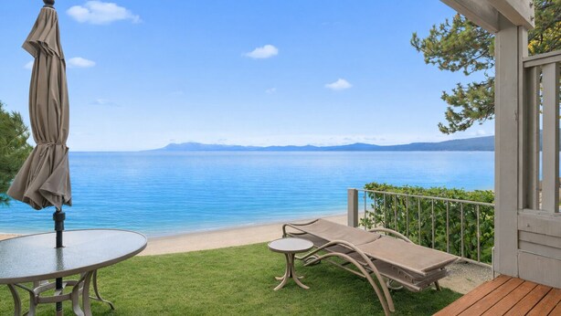 Un balcón con vistas al mar tranquilo, una mesa con sombrilla y dos sillones de relax.