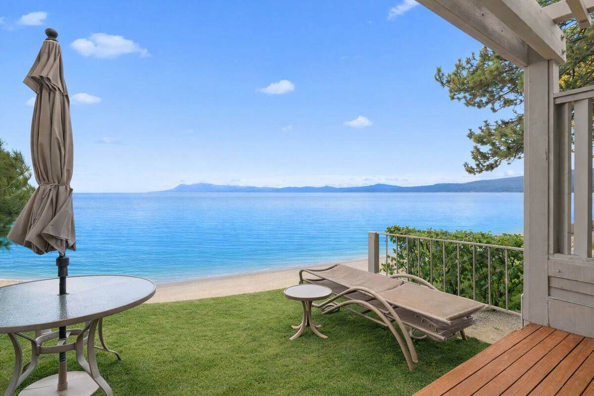 A balcony with a view of a calm sea, a table with an umbrella, and two lounge chairs.