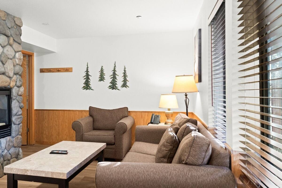 A cozy living room with a stone fireplace, a comfortable sofa, a wooden coffee table, and a lamp.