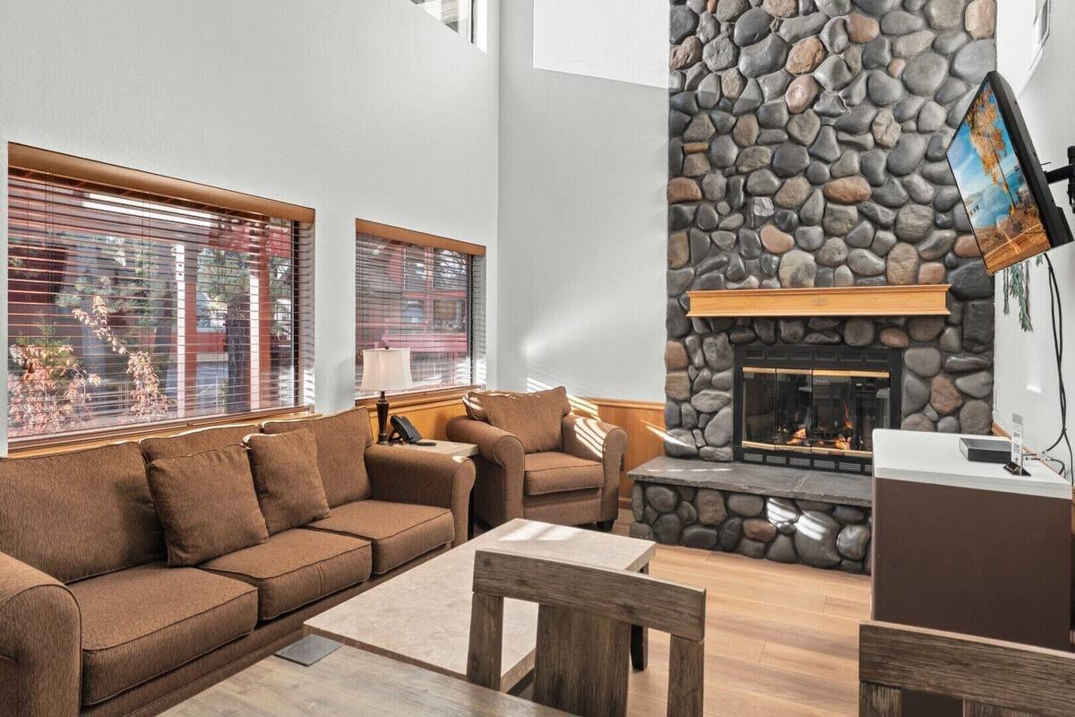 A living room with a stone fireplace, a sofa, a coffee table, and a television mounted on the wall.
