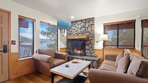 Una sala de estar con chimenea de piedra, dos sofás, una mesa de centro y un televisor montado en la pared.