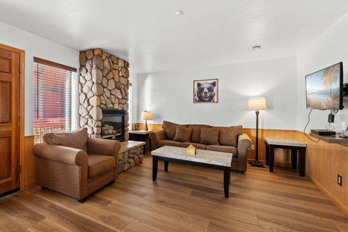 A cozy living room with a stone fireplace, wooden furniture, and a television.