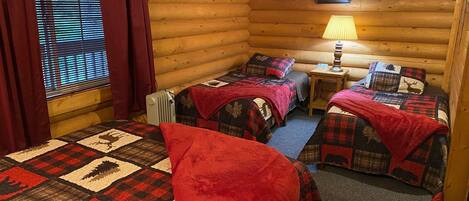 Ein Blockhaus-Zimmer mit zwei Betten, einem fenster mit Vorhängen, einem Heizkörper und einer Lampe.
