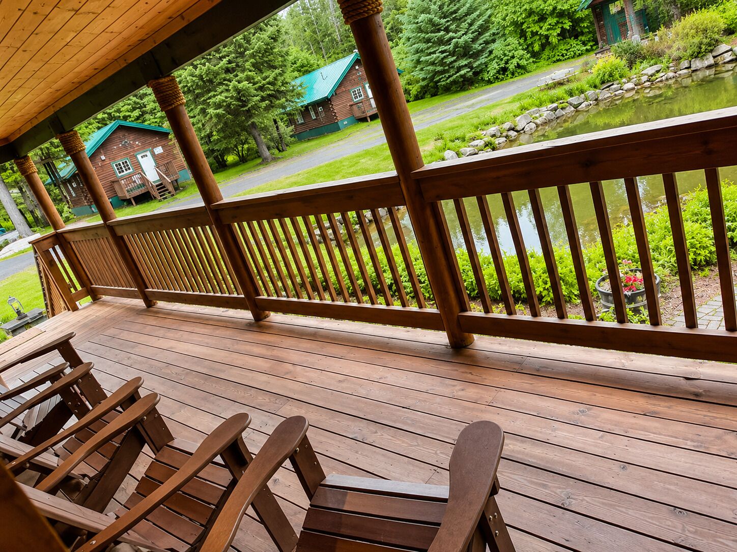 A wooden deck with chairs, a view of a cabin, and a pond.