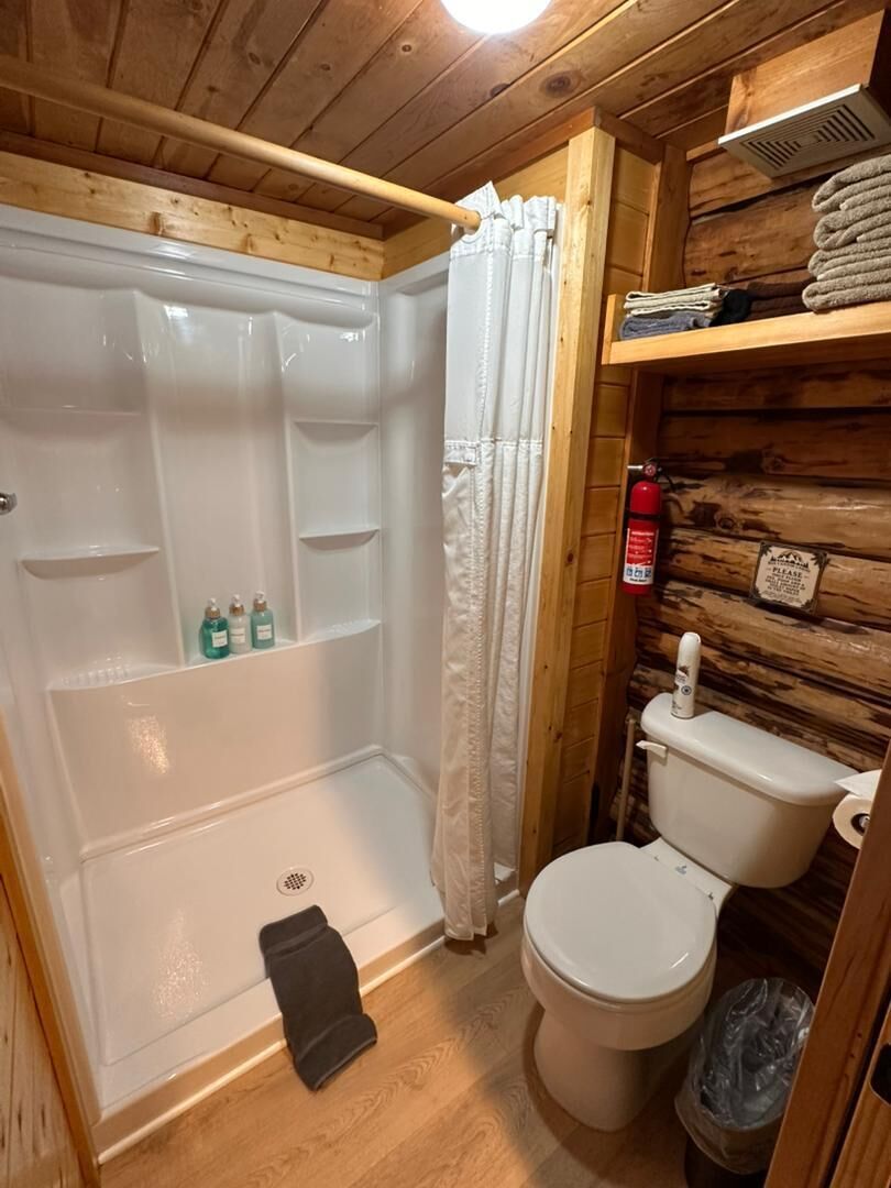 A wooden cabin bathroom with a shower, toilet, and shelves with toiletries.