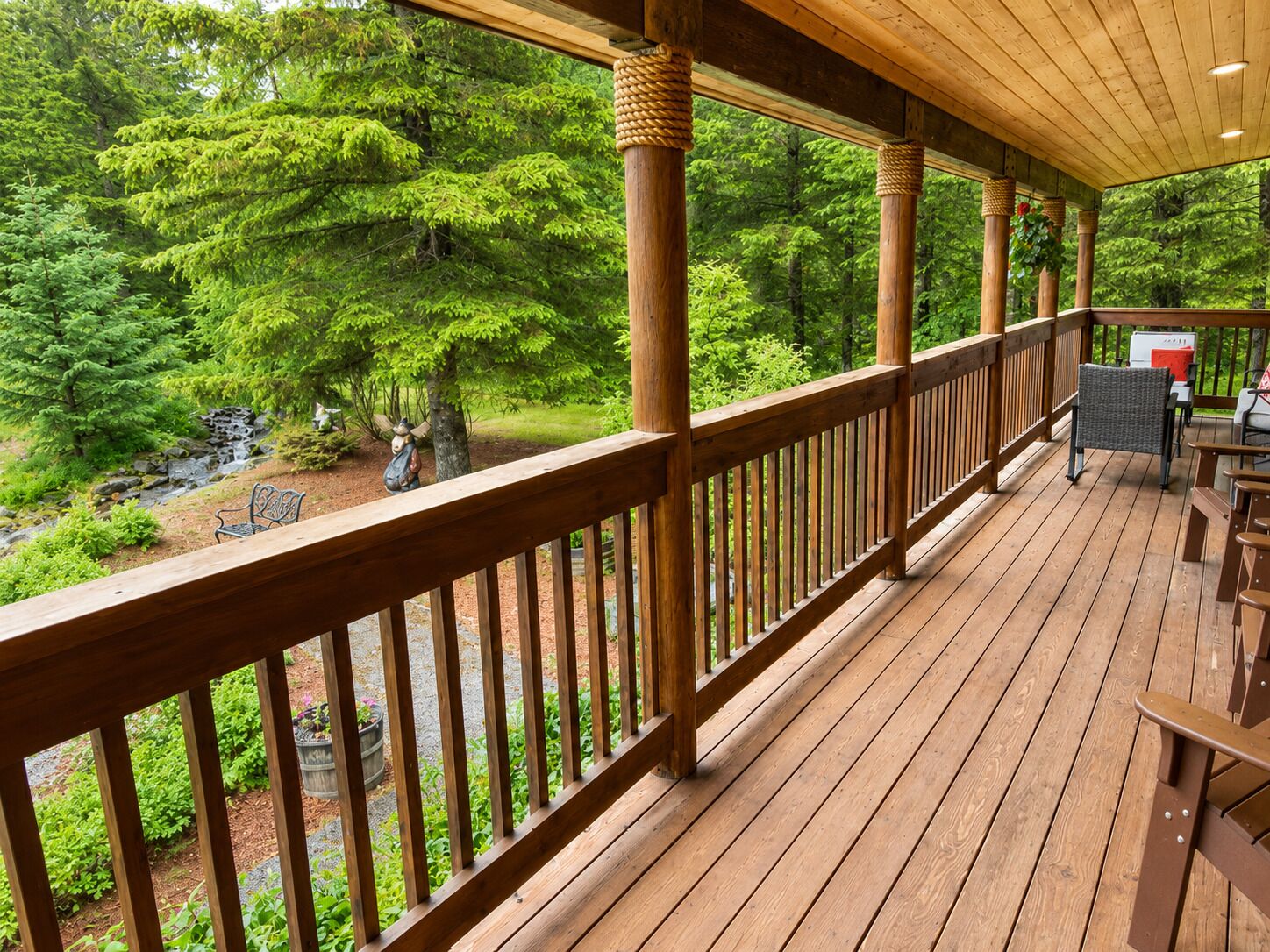 A wooden deck with a railing, outdoor seating, and a view of a forested area.
