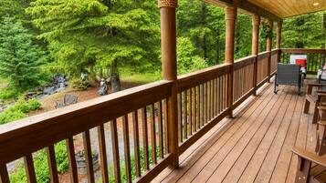 A wooden deck with a railing, outdoor seating, and a view of a forested area.