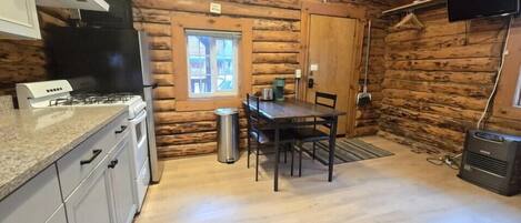 A log cabin interior with a kitchen area, a dining table, and a TV mounted on the wall.