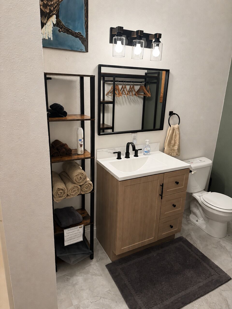 Ein Badezimmer mit einem weißen Waschbecken, einer Holzkommode, einem Handtuchhalter und einem Bild an der Wand.