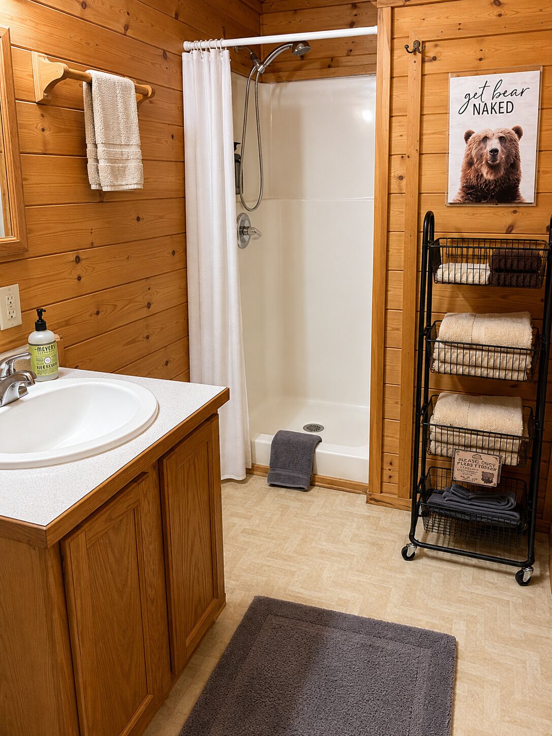 Une salle de bain rustique, aménagée dans une cabane en bois, avec un lavabo, une douche, un porte-serviettes et une affiche représentant un ours.