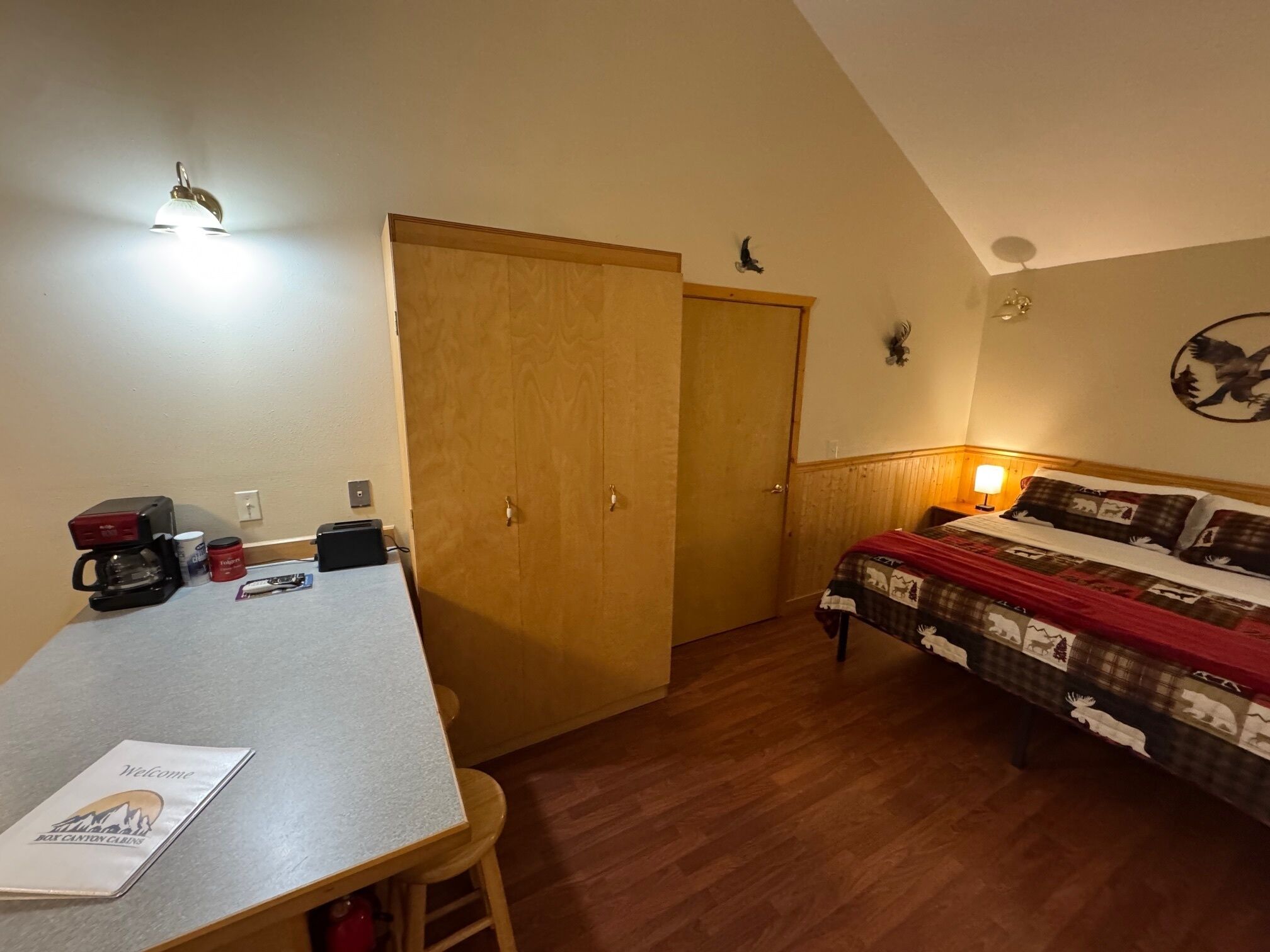 A room with a bed, a desk, a coffee maker, and a wall-mounted light.