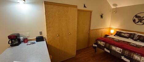 A room with a bed, a desk, a coffee maker, and a wall-mounted light.