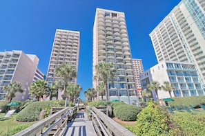 A modern hotel with multiple high-rise buildings, a wooden boardwalk, and well-maintained greenery. - Suites at the Beach (Myrtle Beach)