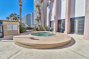 Uma área de piscina com hidromassagem, palmeiras e um edifício com varandas.
