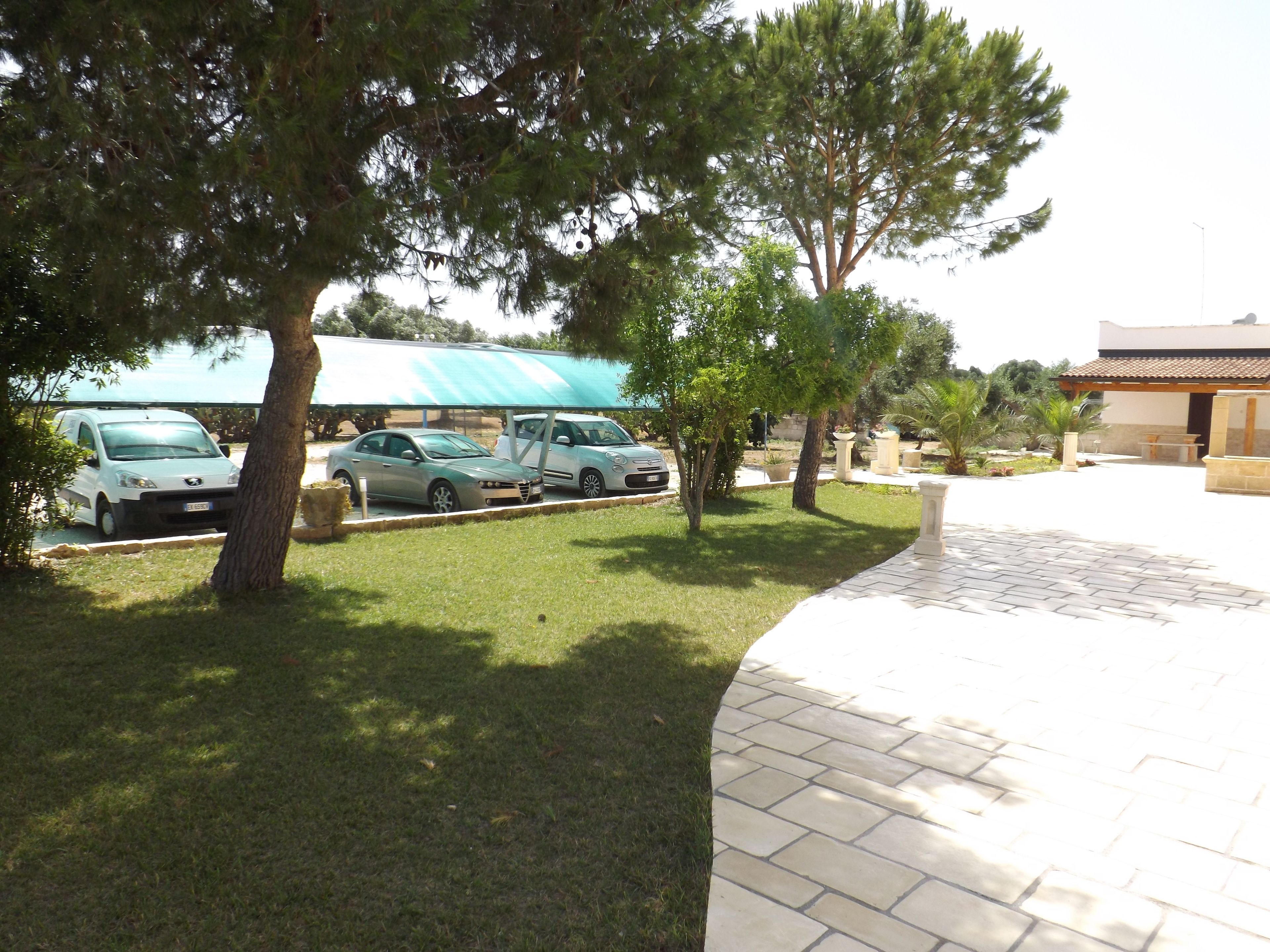 A parking area with several cars, a covered area, and a building with a tiled roof.